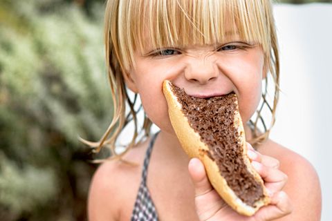 Ein Kind beißt in ein Brot mit einer dunklen Creme drauf