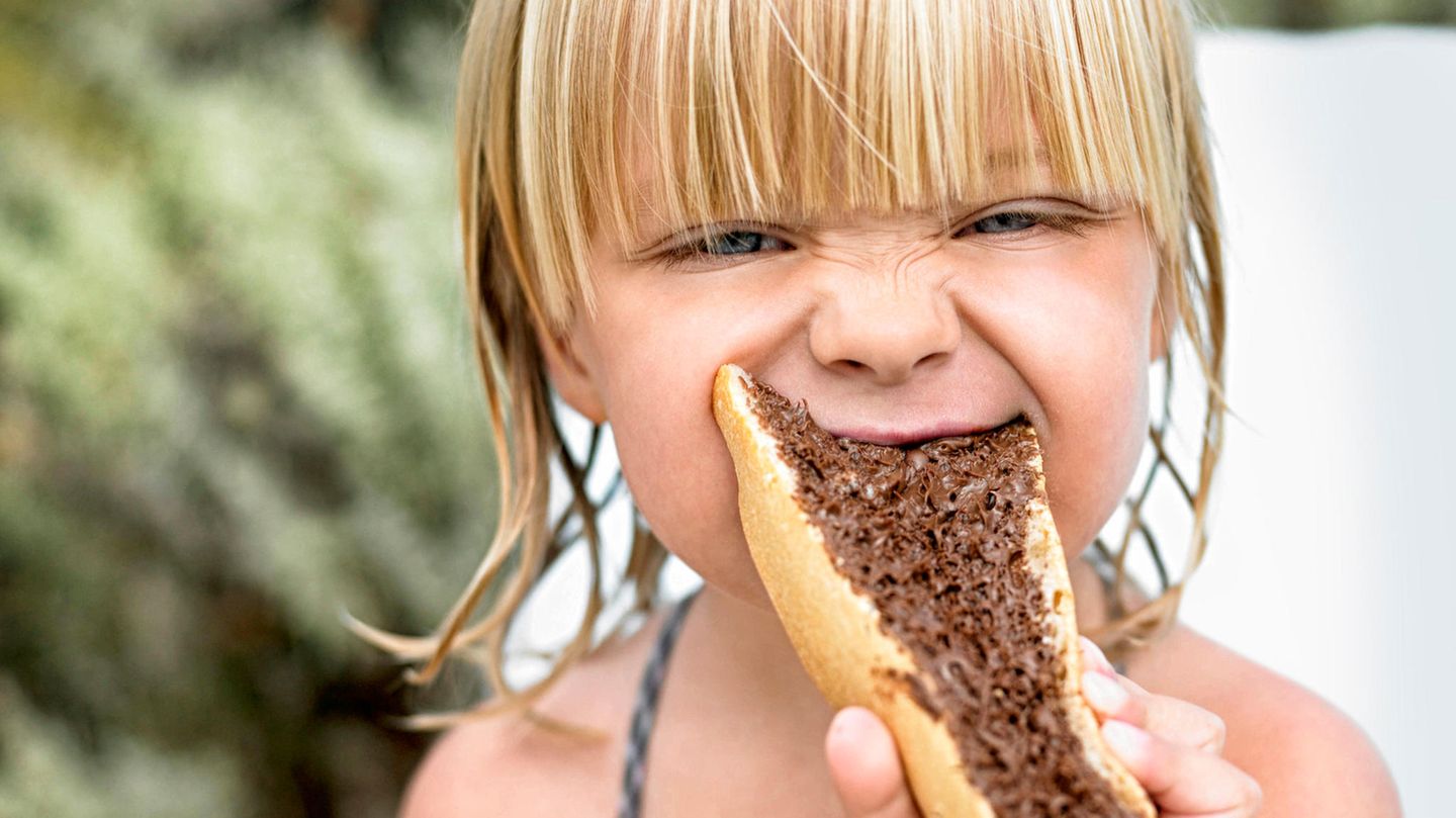 The child bites into a piece of bread with dark cream on it