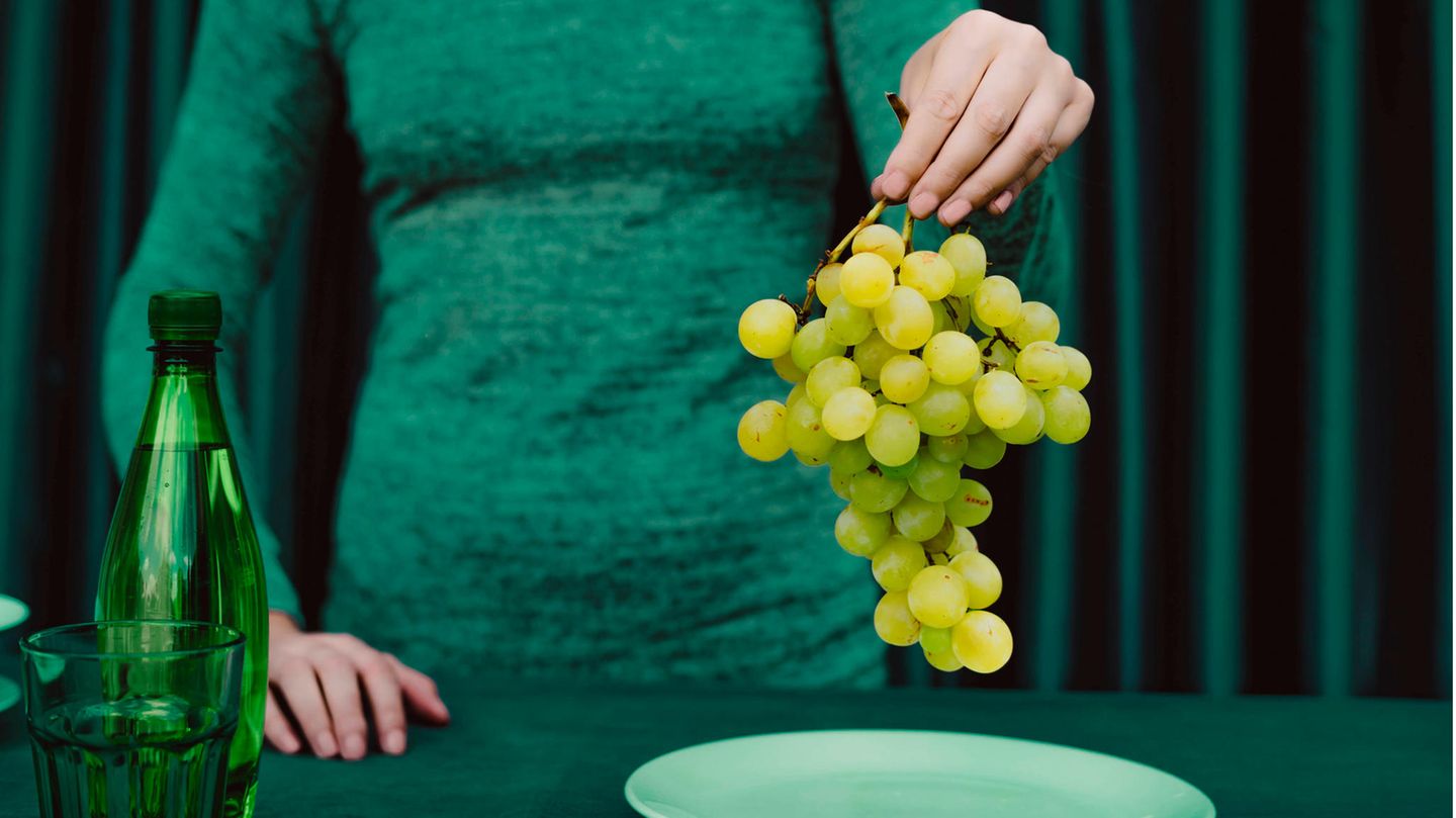 Eine Frau in grün hält einen Strang Weintrauben