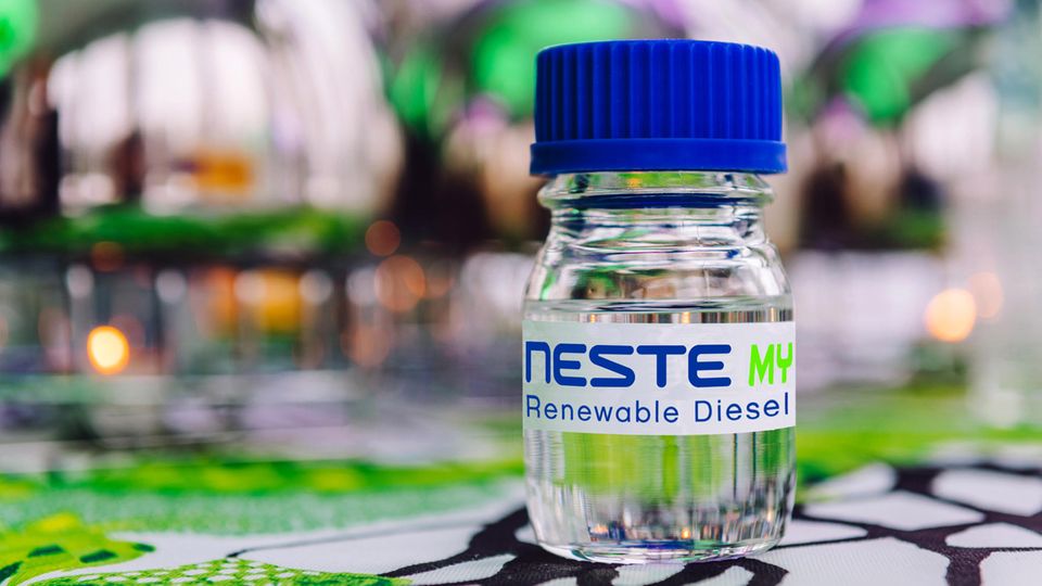 Im Bildvordergrund ist eine Flasche mit einer durchsichtigen Flüssigkeit und der Aufschrift "Neste MY Renewable Diesel" zu sehen
