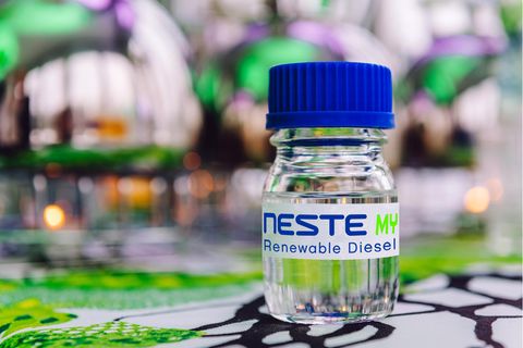 Im Bildvordergrund ist eine Flasche mit einer durchsichtigen Flüssigkeit und der Aufschrift "Neste MY Renewable Diesel" zu sehen
