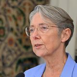 Eine ältere weiße Frau mit kurzen, grauen Haaren und randloser Brille spricht in ein Mikrofon