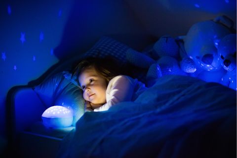 Nachtlicht für Kinder: Kleines Mädchen liegt mit einem Nachtlicht im Bett