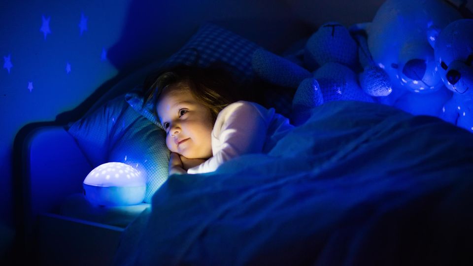 Nachtlicht für Kinder: Kleines Mädchen liegt mit einem Nachtlicht im Bett