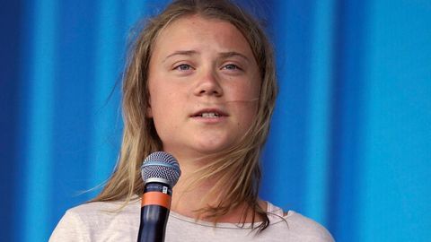 Eine junge weiße Frau mit rundlichen Gesicht und langen dunkelblonden Haaren spricht auf einer Bühne in ein Mikro in ihrer Hand