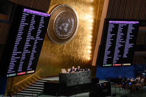 Neben einer goldenen Wand mit UN-Wappen zeigen große Monitore das Abstimmungsergebnis