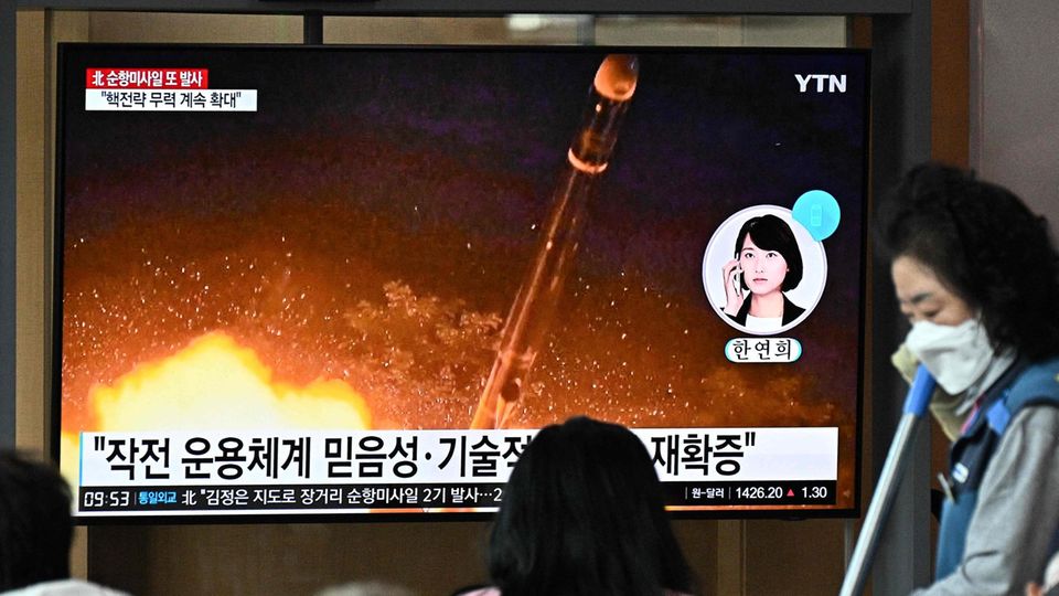 Ein schwarzhaariges Mädchen sitzt vor einem Fernseher, auf dem eine Rakete startet. Auf dem Bildschirm sind koreanische Zeichen