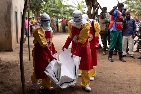 Mitarbeiter des Roten Kreuzes in Uganda in Schutzanzügen transportieren einen Leichensack aus einem Dorf
