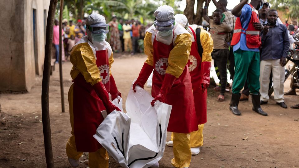 Mitarbeiter des Roten Kreuzes in Uganda in Schutzanzügen transportieren einen Leichensack aus einem Dorf