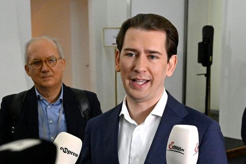 Ein junger weißer Mann in blauem Anzug und weißem Hemd spricht in Mikrofone unterschiedlicher TV-Sender