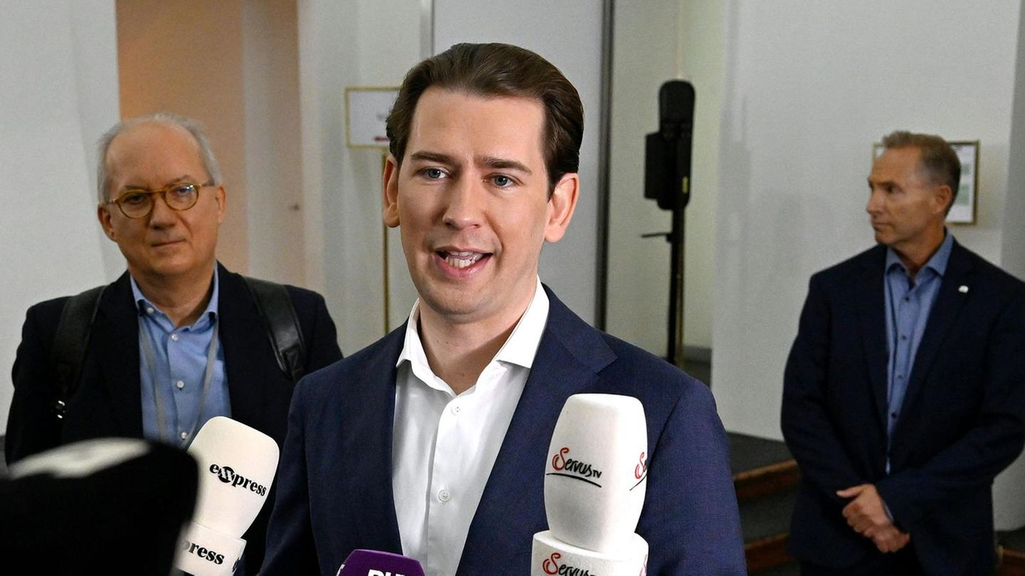 Ein junger weißer Mann in blauem Anzug und weißem Hemd spricht in Mikrofone unterschiedlicher TV-Sender