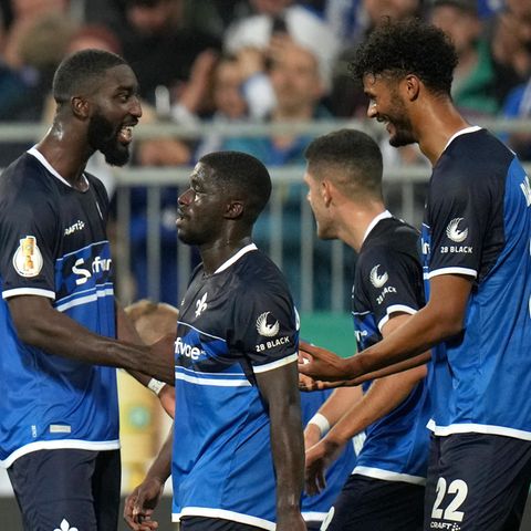 Vier Fußballer in blauen Trikots und Hosen bejubeln gemeinsam ein Tor