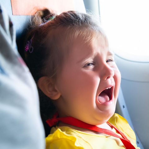 Kleinkind sitzt in einem Flugzeug und schreit
