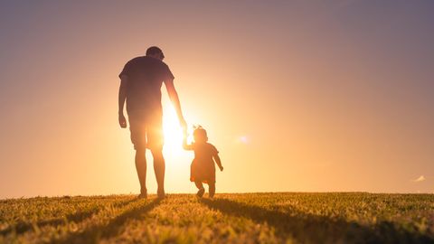 Ein Vater geht mir seiner Tochter im Sonnenuntergang spazieren.