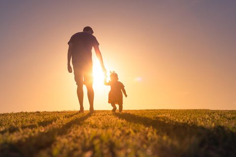 Ein Vater geht mir seiner Tochter im Sonnenuntergang spazieren.