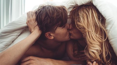 Ein Mann und eine Frau küssen sich unter der Bettdecke.