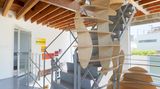 Entlang der Treppe schlängelt sich eine Kunstinstallation aus Holz vom ersten Stockwerk bis in die oberste Etage. Diese dient neben der Optik auch praktischen Zwecken: als Regalfläche und Stauraum in dem nicht gerade einfach zu möblierenden Haus.