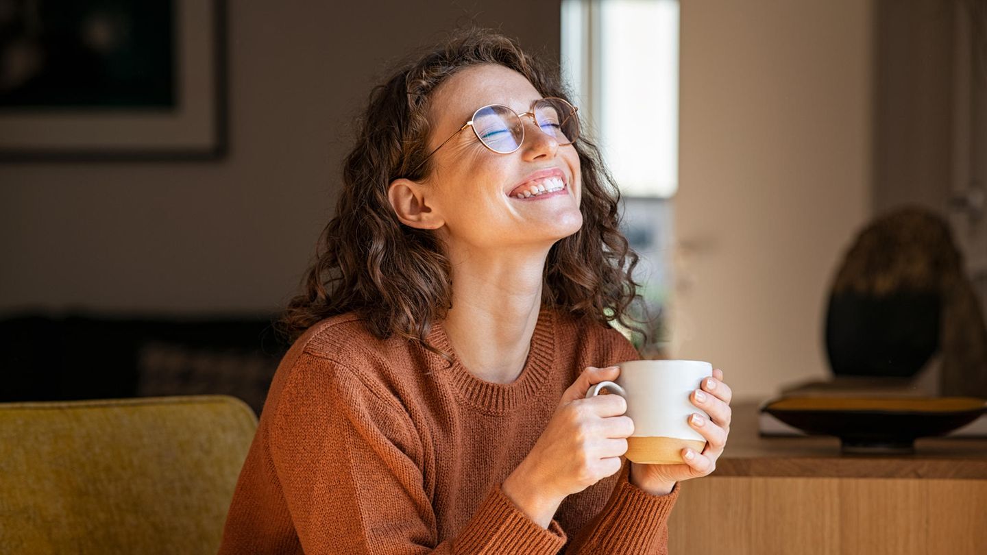 Eine Frau lächelt mit geschlossenen Augen und einer Tasse Tee in der Hand.