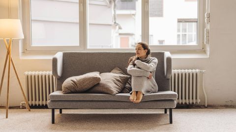 Eine Frau sitzt mit angezogenen Beinen auf einem Sofa