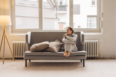 Eine Frau sitzt mit angezogenen Beinen auf einem Sofa