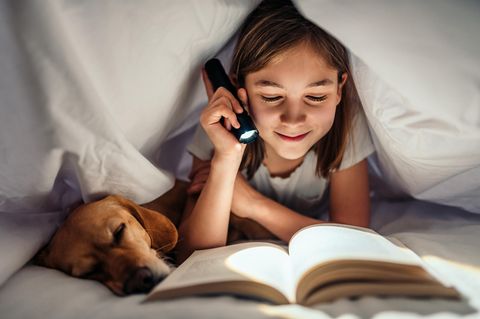 Ein Mädchen liest unter der Bettdecke