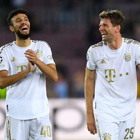 Zwei Fußball-Profis in weißen Trikots und Hosen gehen lachend nebeneinander über den Platz