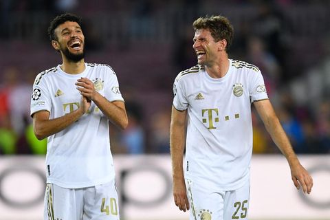 Zwei Fußball-Profis in weißen Trikots und Hosen gehen lachend nebeneinander über den Platz