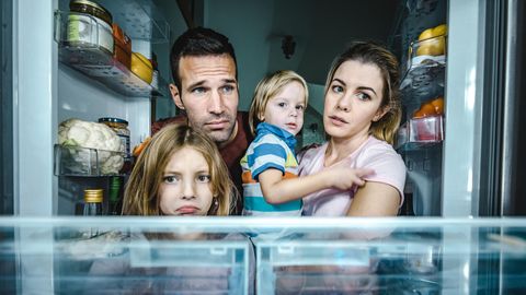 Eine Familie schaut traurig in einen leeren Kühlschrank