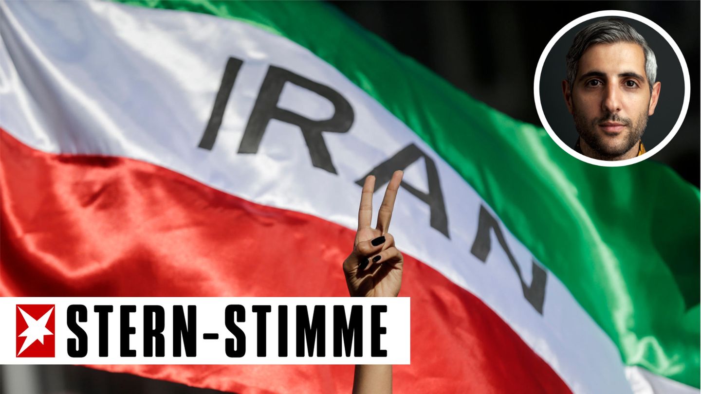 Eine Frau zeigt auf einer Demonstration für die Menschenrechte im Iran das Victory-Zeichen vor einer iranischen Fahne