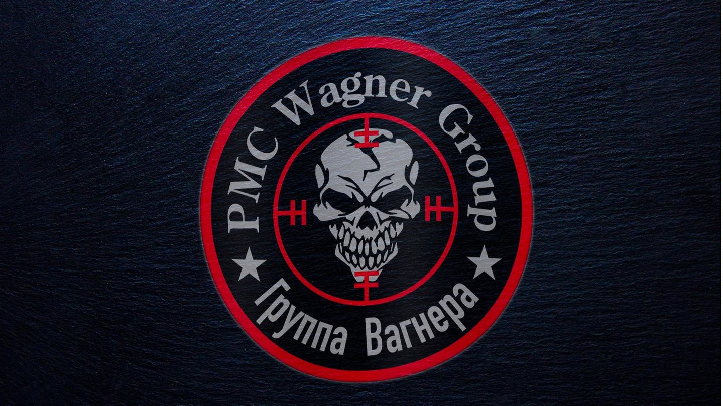 Ein rundes Logo zeigt in roter Umrandung einen grinsenden Totenschädel in einem Fadenkreuz unter der Schrift "PMC Wagner Group"