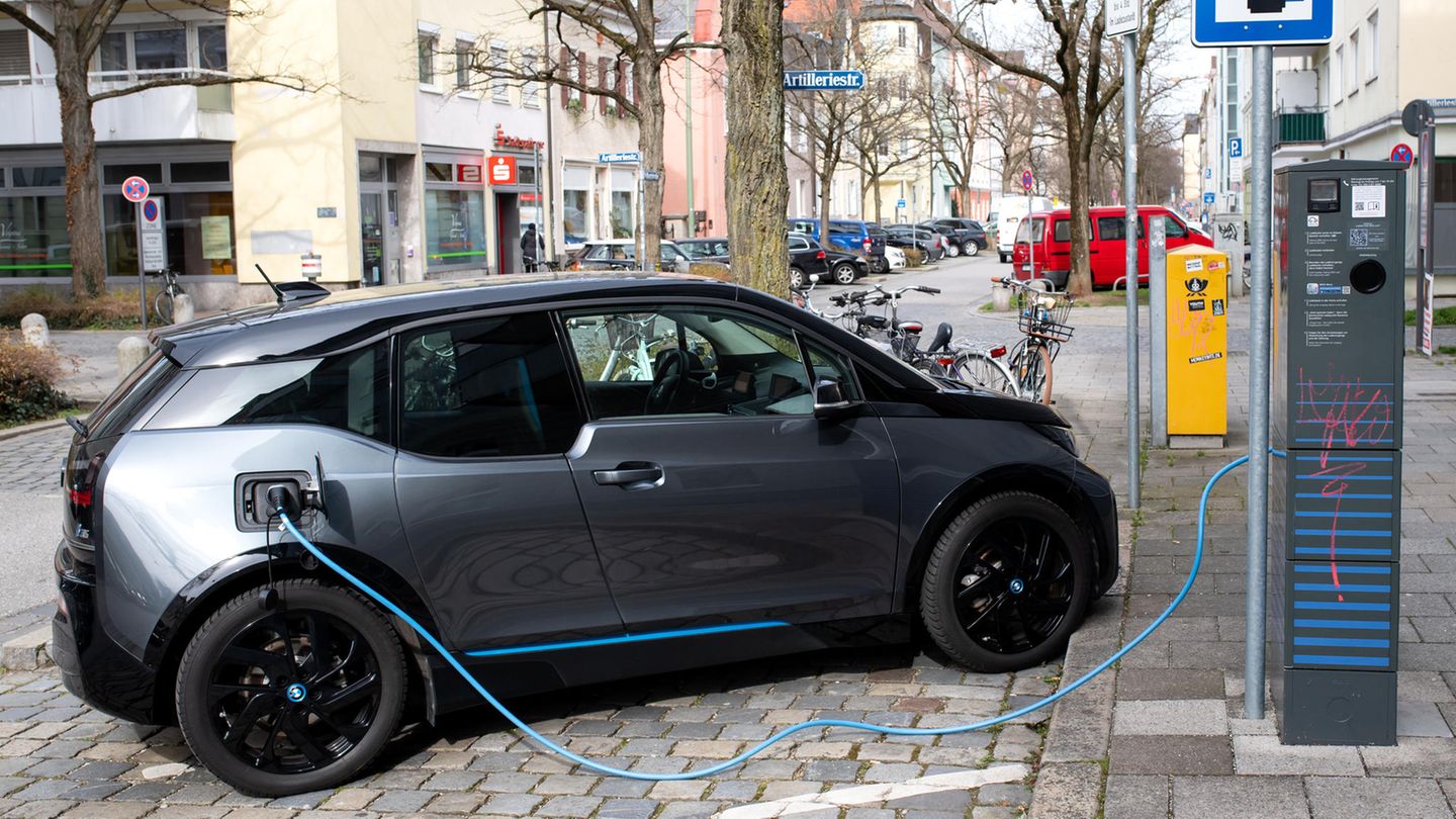 Ein elektrischer Kompaktwagen steht in einer Parkbucht mit Ladesäule. Ein blaues Kabel führt zum Heck des Autos