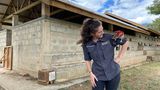 Eine Frau steht vor einem Gebäude aus Steinen und schaut eine Ratte an, die auf ihrer Schulter sitzt