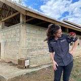 Eine Frau steht vor einem Gebäude aus Steinen und schaut eine Ratte an, die auf ihrer Schulter sitzt