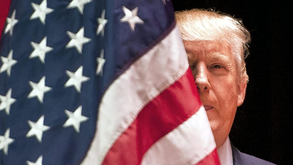 Donald Trump halb versteckt hinter einer US-Flagge
