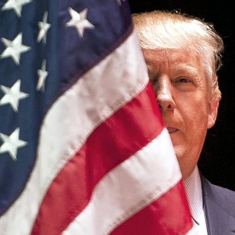 Donald Trump halb versteckt hinter einer US-Flagge