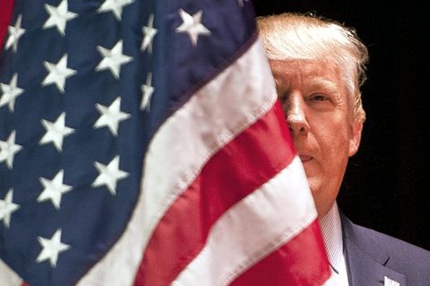 Donald Trump halb versteckt hinter einer US-Flagge