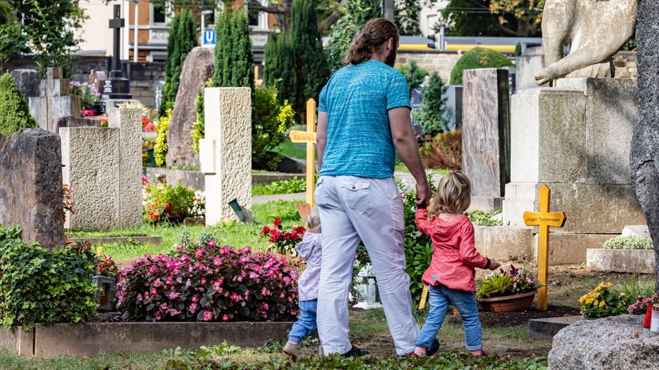 Kinder Tod Eltern Beerdigung Ein Mann geht mit zwei Kindern an der Hand über den Friedhof