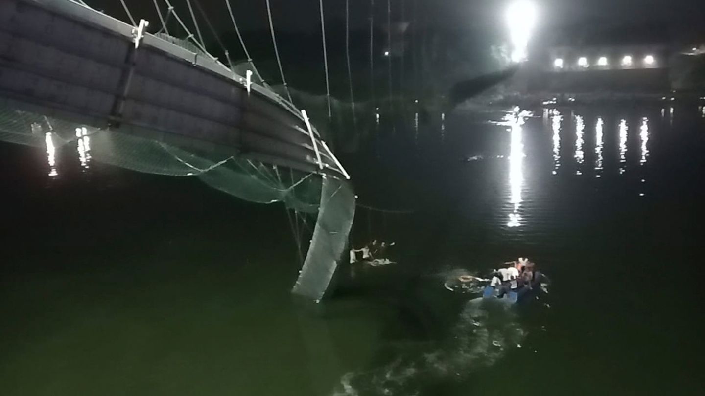 Rettungshelfer auf Booten suchen im Fluss Machchu neben einer eingestürzten Brücke nach Opfern