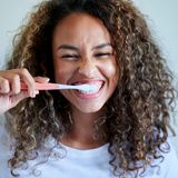 Eine Frau putzt sich lächelnd die Zähne.