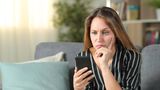 Eine Frau schaut genervt auf ihr Smartphone.