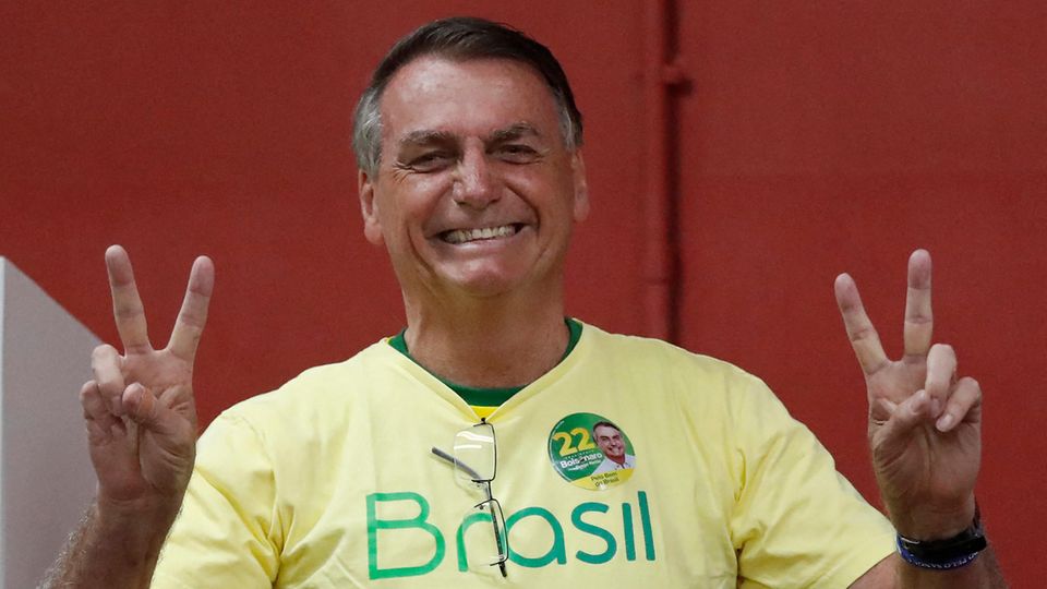 Ein braungebrannter älterer Mann im gelben "Brasil"-T-Shirt macht mit beiden Händen Victory-Zeichen und lächelt breit