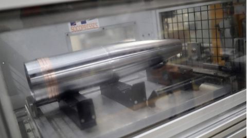 In einer Fabrik ist eine silbern glänzende Granatenhülse in einer Maschine eingespannt