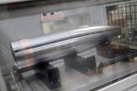 In einer Fabrik ist eine silbern glänzende Granatenhülse in einer Maschine eingespannt