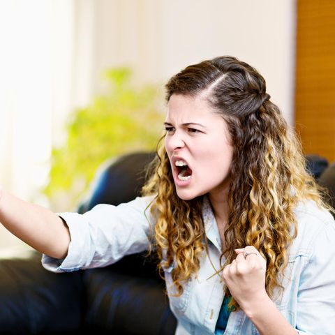 Eine frustrierte Frau sitzt auf der Couch und hält eine Fernbedienung