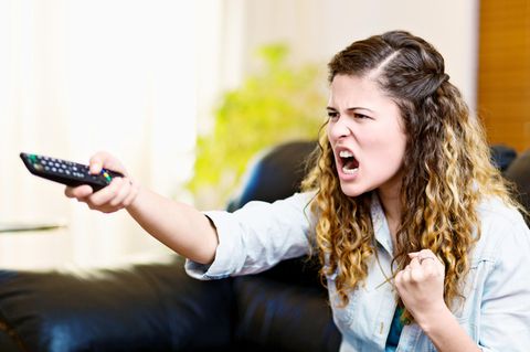 Eine frustrierte Frau sitzt auf der Couch und hält eine Fernbedienung
