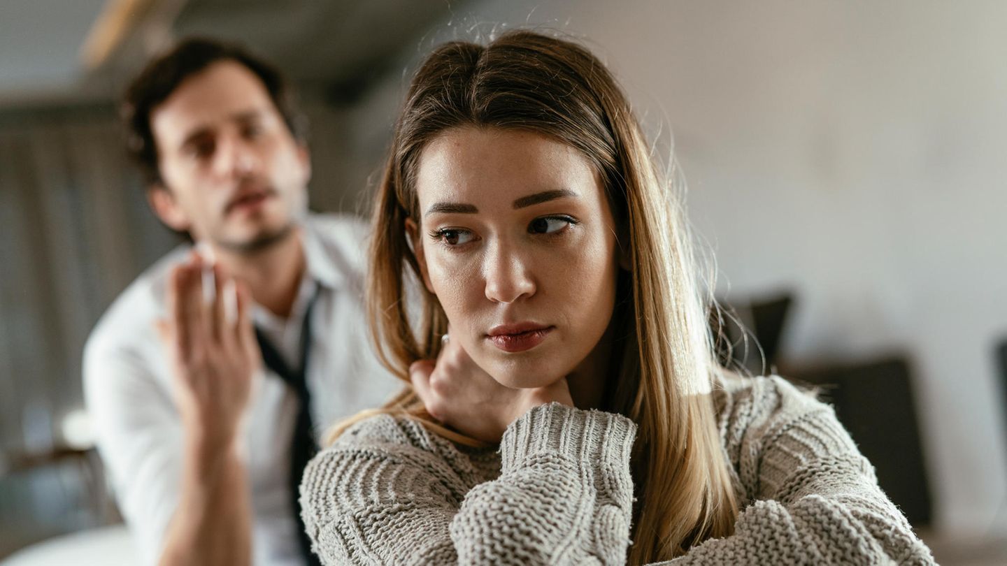 Eine Frau guckt traurig, während ihr Mann im Hintergrund meckert. Eine Frau guckt traurig, während ihr Mann im Hintergrund meckert.