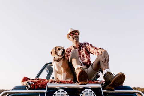 Ein Mann sitzt mit seinem Hund auf einem Auto.