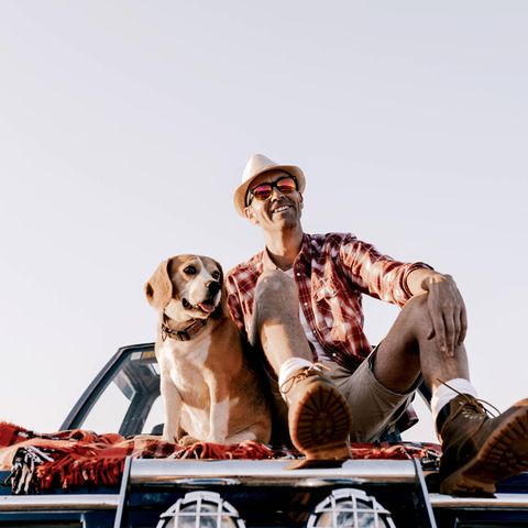 Ein Mann sitzt mit seinem Hund auf einem Auto.