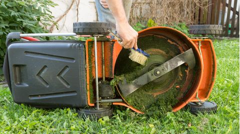 Gartentipps für November: Mnann reinigt Rasenmäher mit einem Handfeger