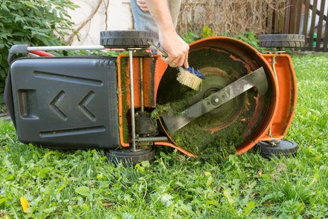 Gartentipps für November: Mnann reinigt Rasenmäher mit einem Handfeger